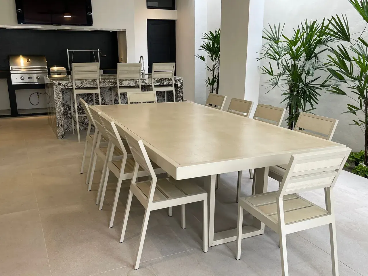 Mesa de jardín Mishka Garden de gran formato con sillas, junto a una cocina exterior