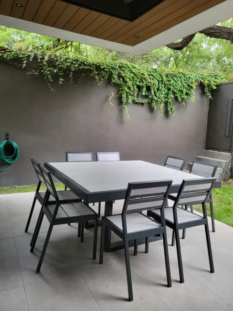 Comedor de exterior Mishka Garden con ocho sillas en un patio con enredadera
