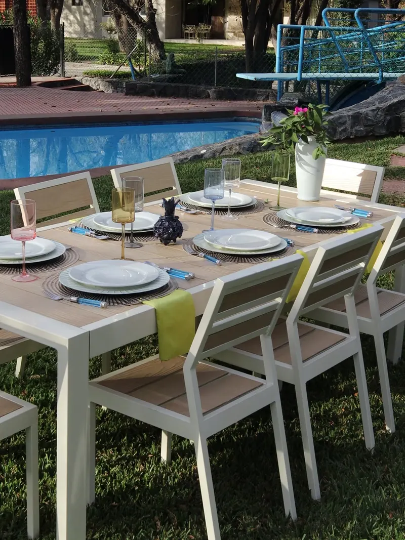 Mesa de exterior puesta con vajilla y sillas claras junto a una alberca