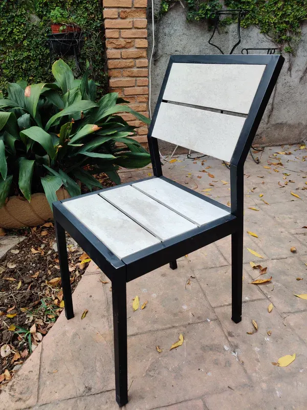 Silla de jardín Mishka Garden, de acero negro y tabletas claras, en un patio con plantas