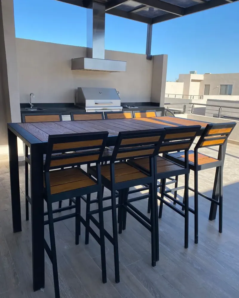 Mesa Akumal con sillas altas en una terraza con asador